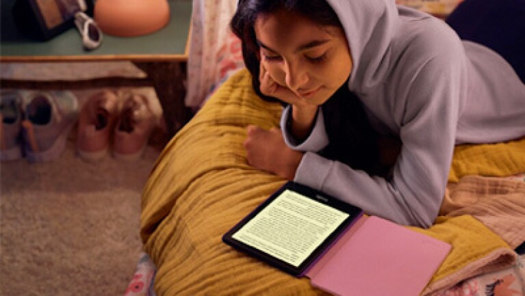 Girl lays on bed while reading an Amazon Kindle.