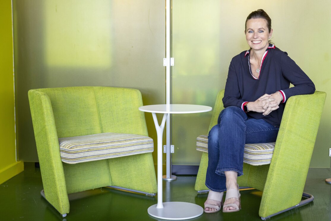 Claire Peters smiles and sits in a modern green chair at an Amazon office.