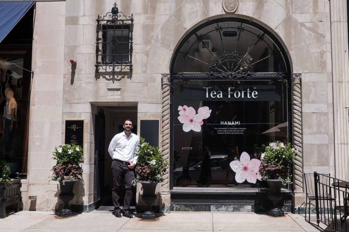 A man in a white button-down shirt stands in front of a storefront with the words "Tea Forté" on it.