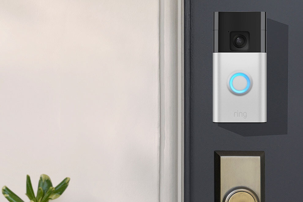 Ringドアベルの本体カラーシルバーが玄関ドアの鍵穴上部に設置され、正面のLEDリングが青く点灯している。