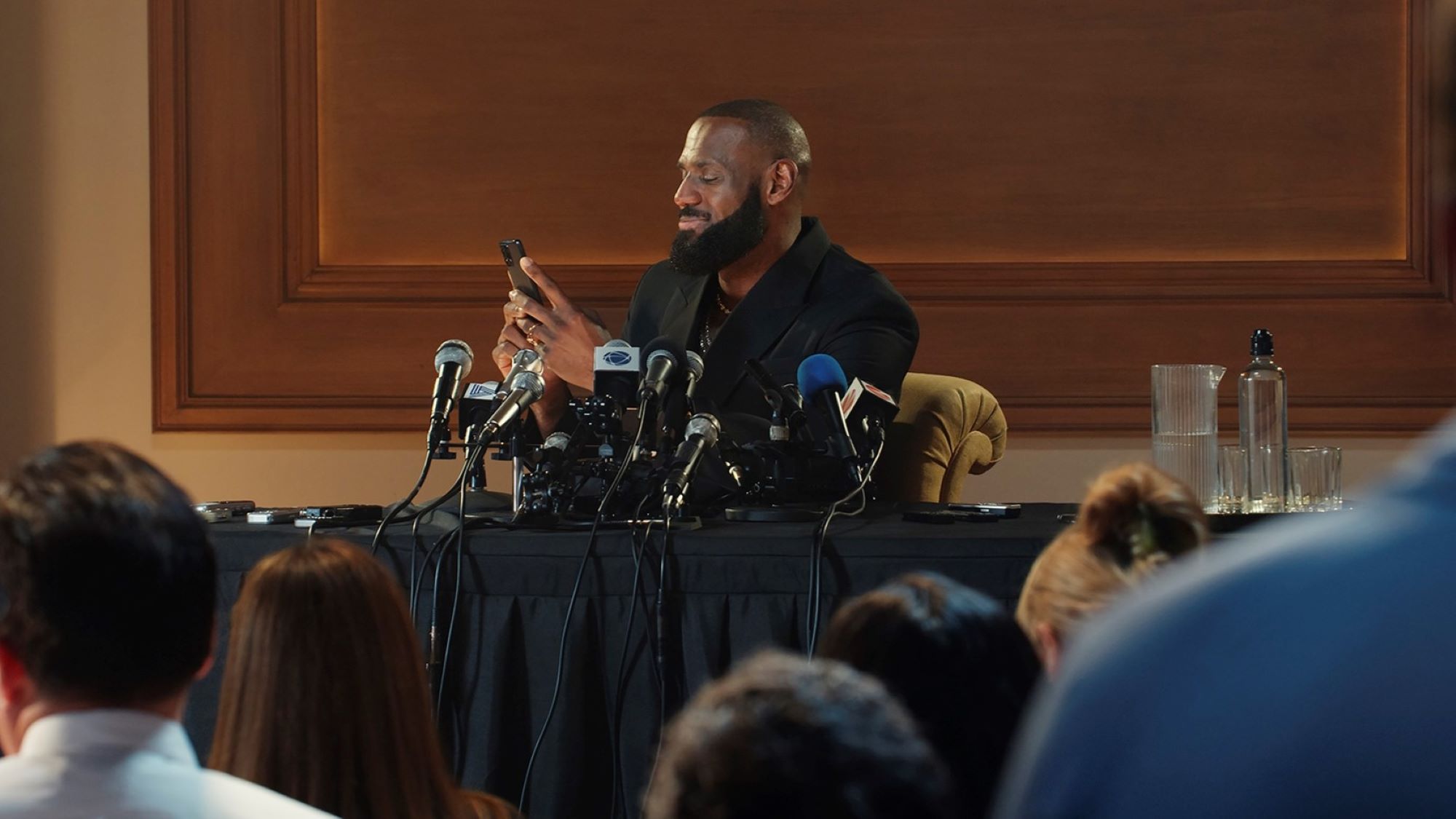 Lebron James checks phone during press conference with multiple microphones