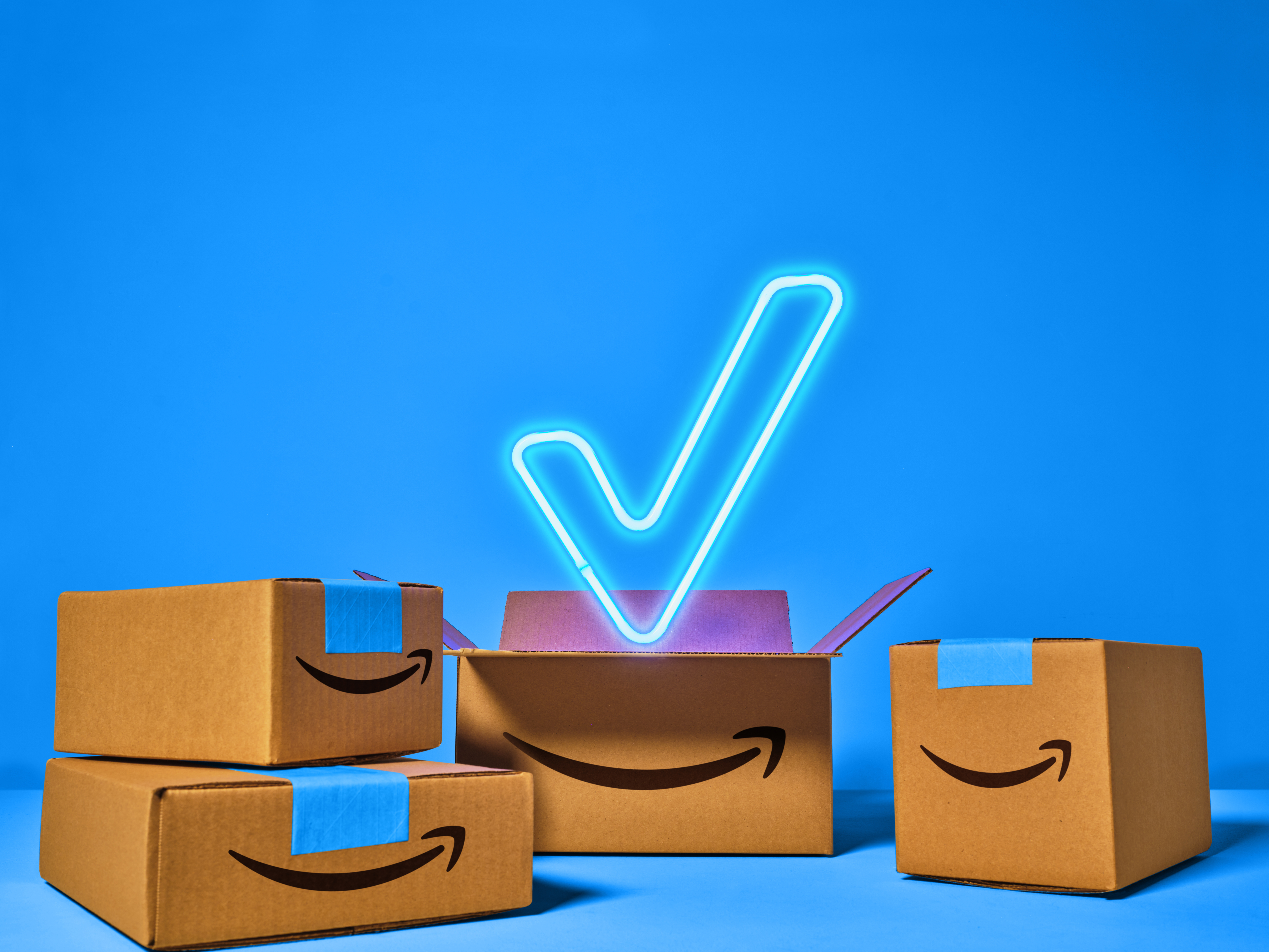 verschiedene Amazon Pakete mit Logo vor einem blauen Hintergrund. Über ihnen ist ein Häkchen.