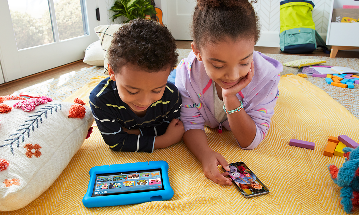 Two young kids plating on their respective devices: a kindle and a phone