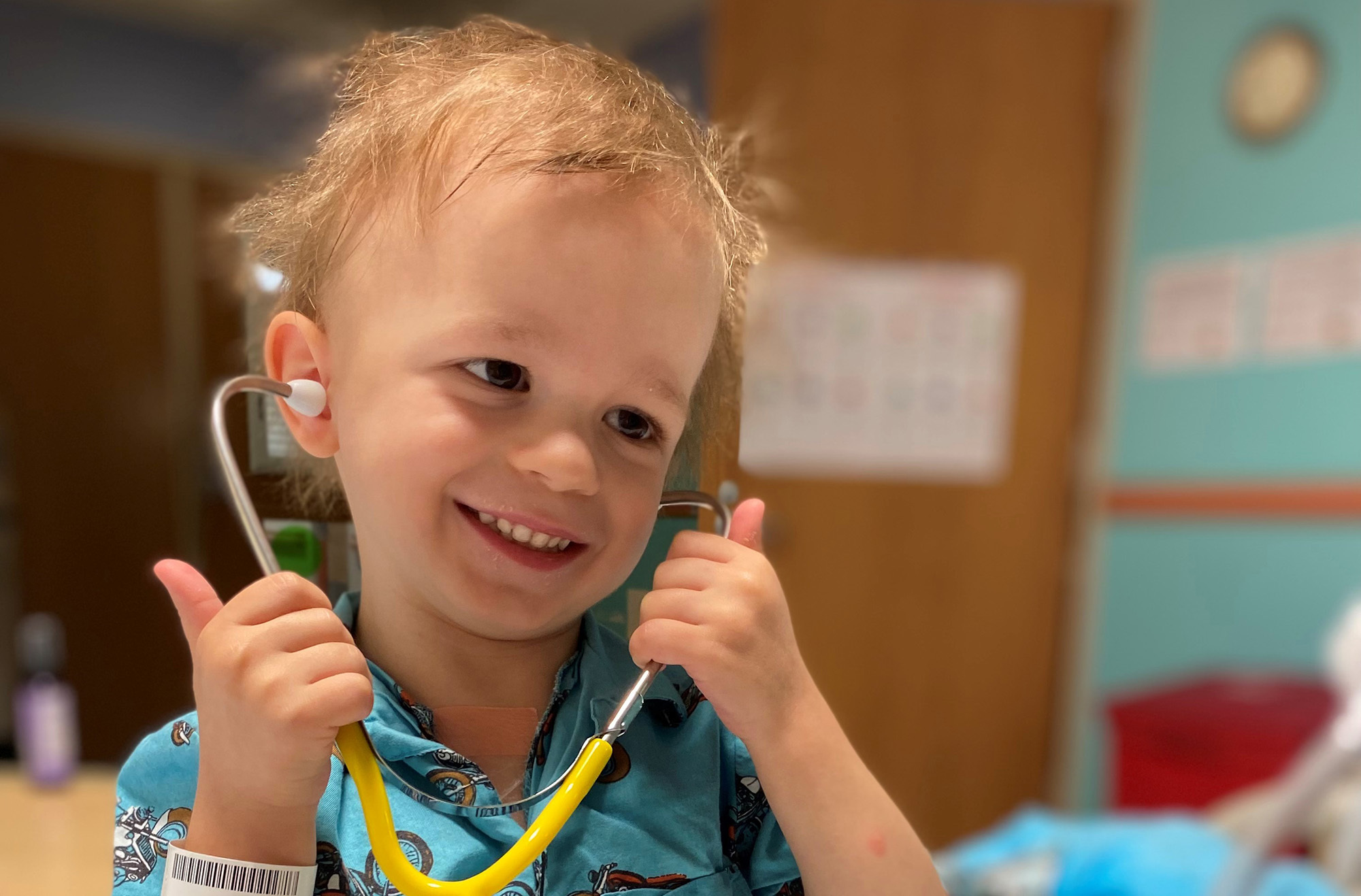 An image of a young boy smiling while hold a stethoscope to his ears.