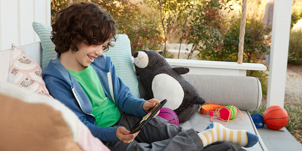 Child sitting on porch, smiling while viewing content on his tablet.