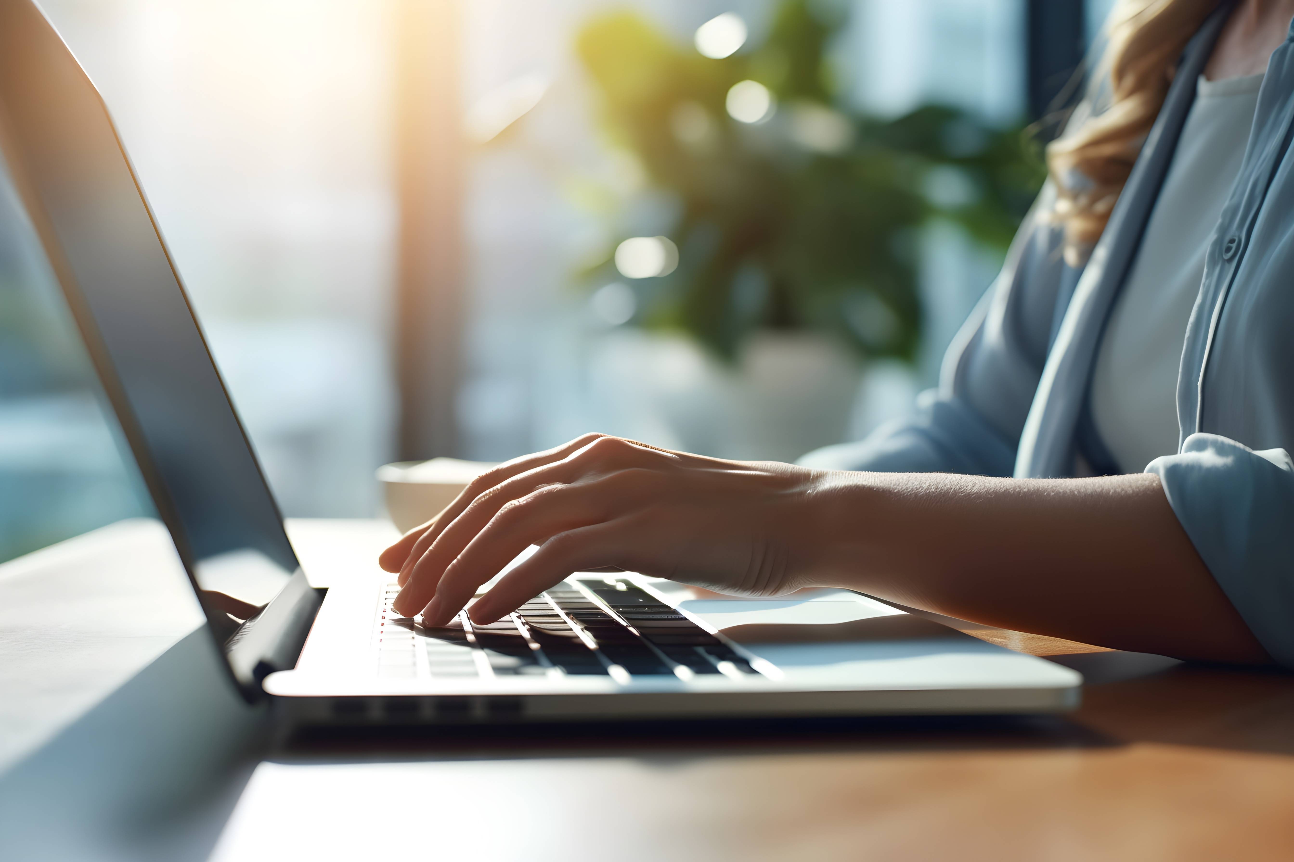 窓の近くに座っている女性がPCでタイピングしている。