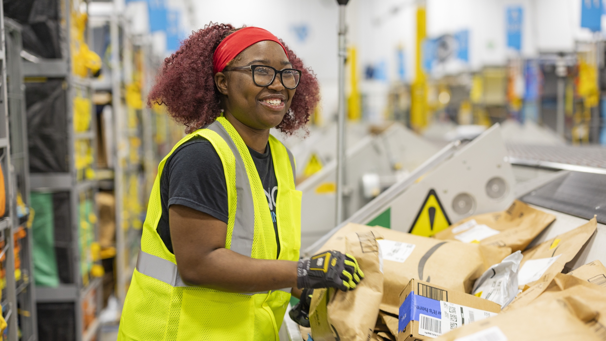Smiling woman wearing glasses and red headband working in Amazon fulfillment facility