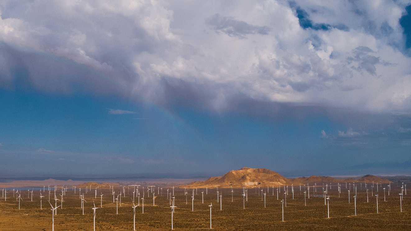 広大な荒れ地に、無数の風力発電ファンが立っている。空には分厚い雲が浮かび、薄い虹が見える。