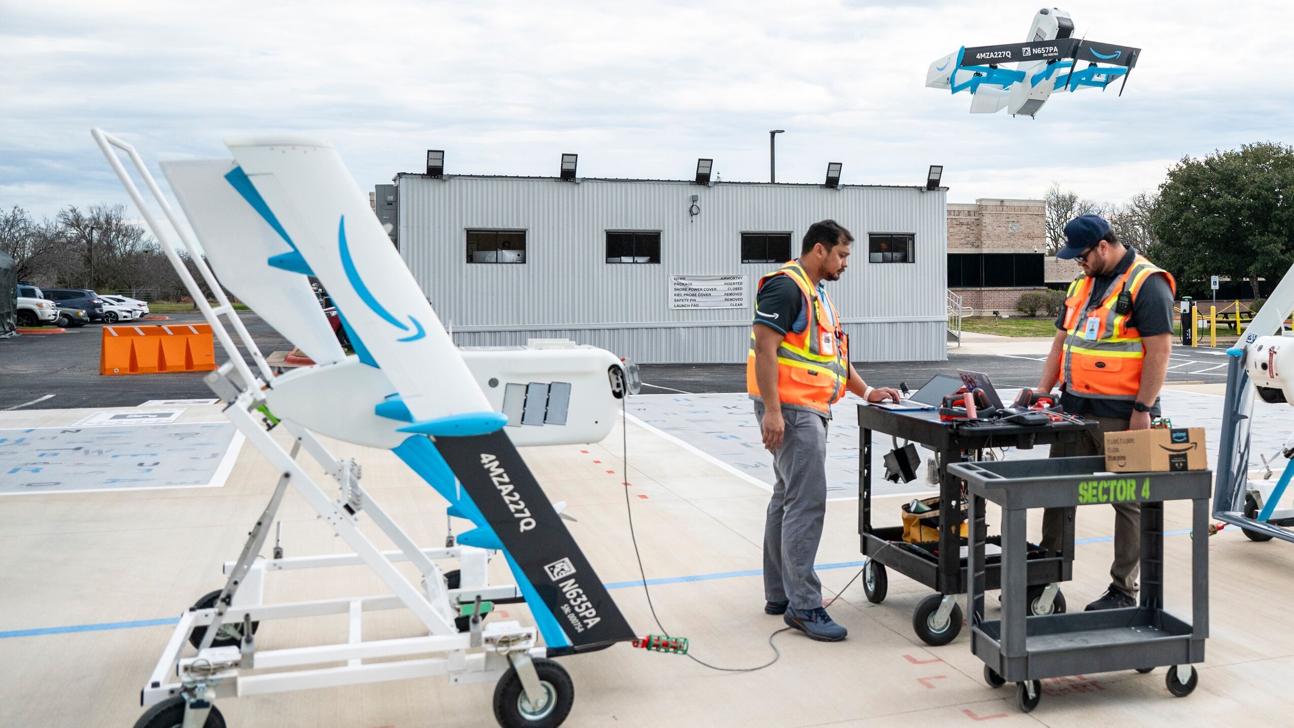 Two Amazon employees stand on the launch pad for the delivery drones to monitor the drone's takeoff