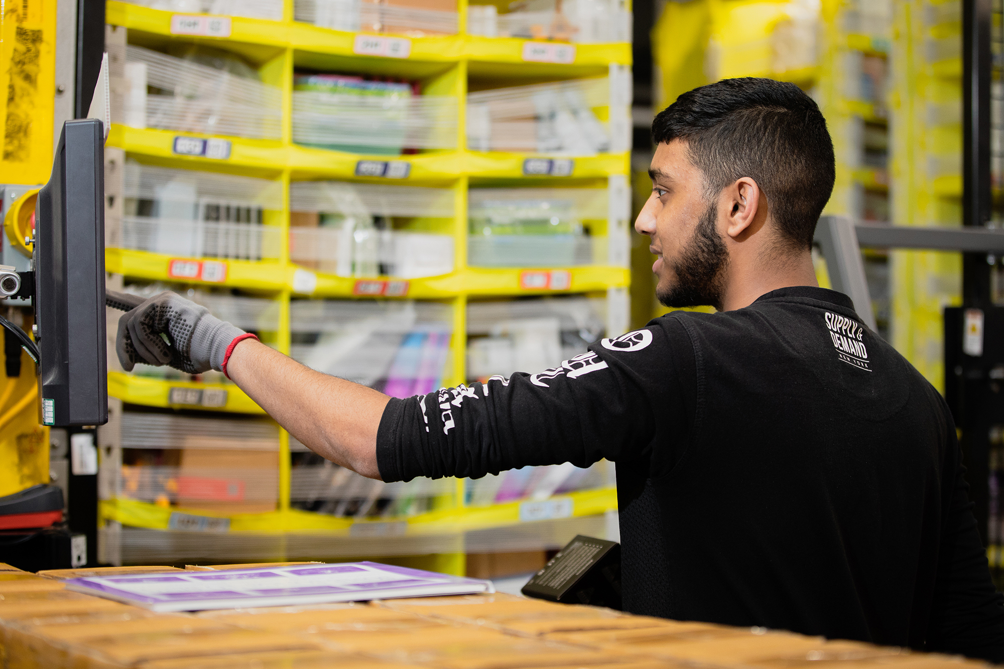 A man at an Amazon fulfillment center touches a monitor at his work station