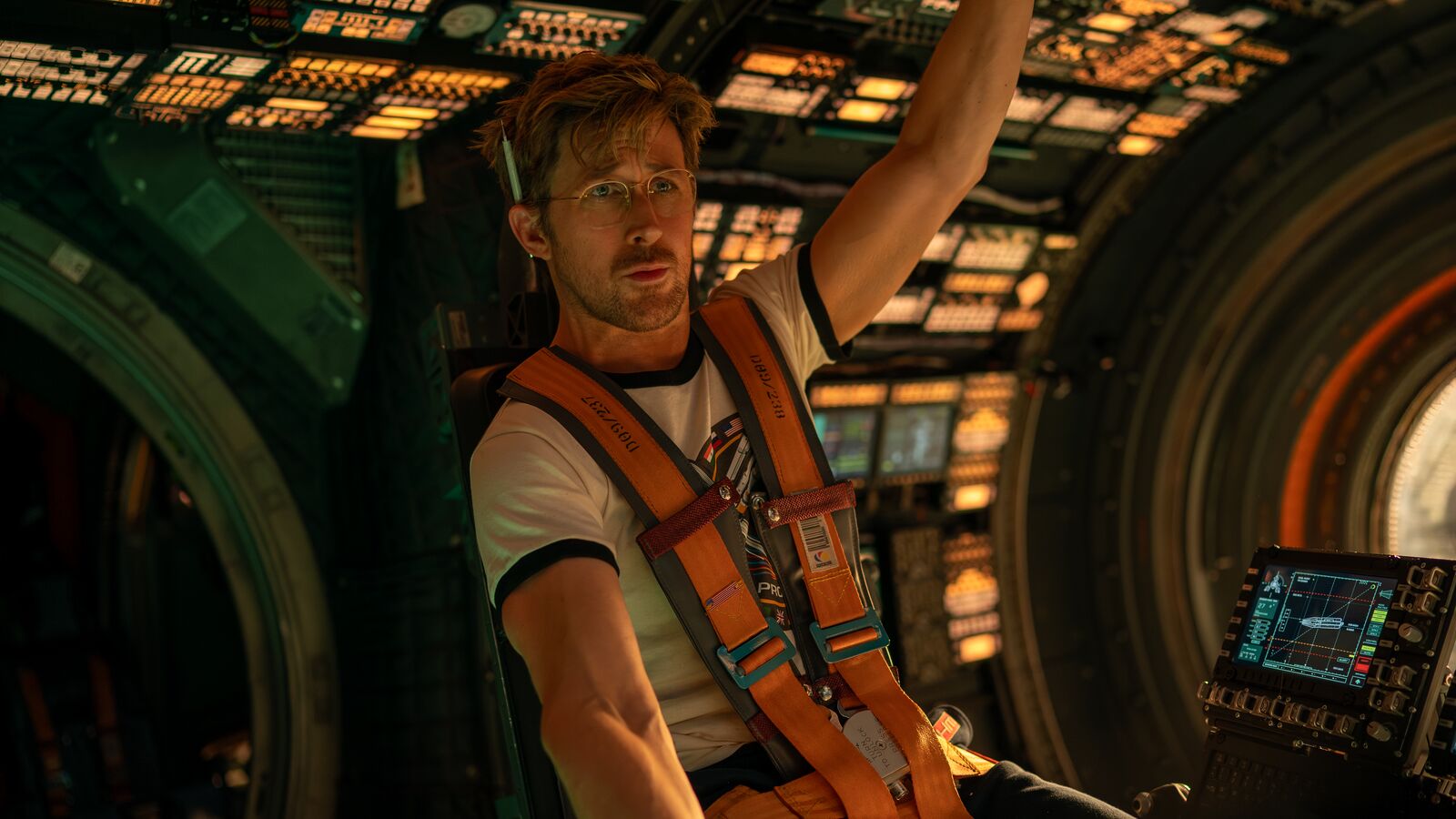 A scene from Project Hail Mary starring Ryan Gosling as Ryland Grace in white shirt with orange harness inside spacecraft