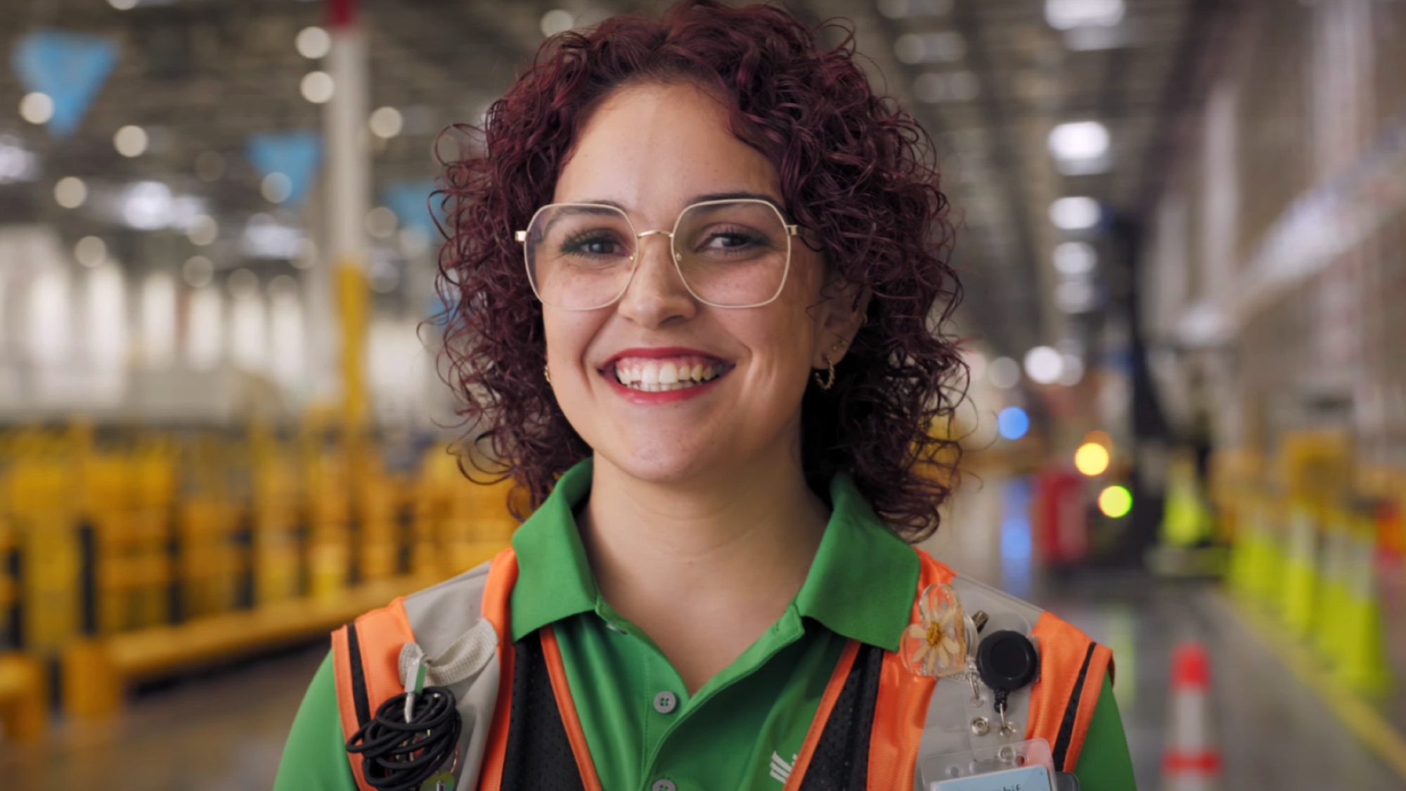 Smiling Amazon employee with curly hair and glasses wearing a safety vest