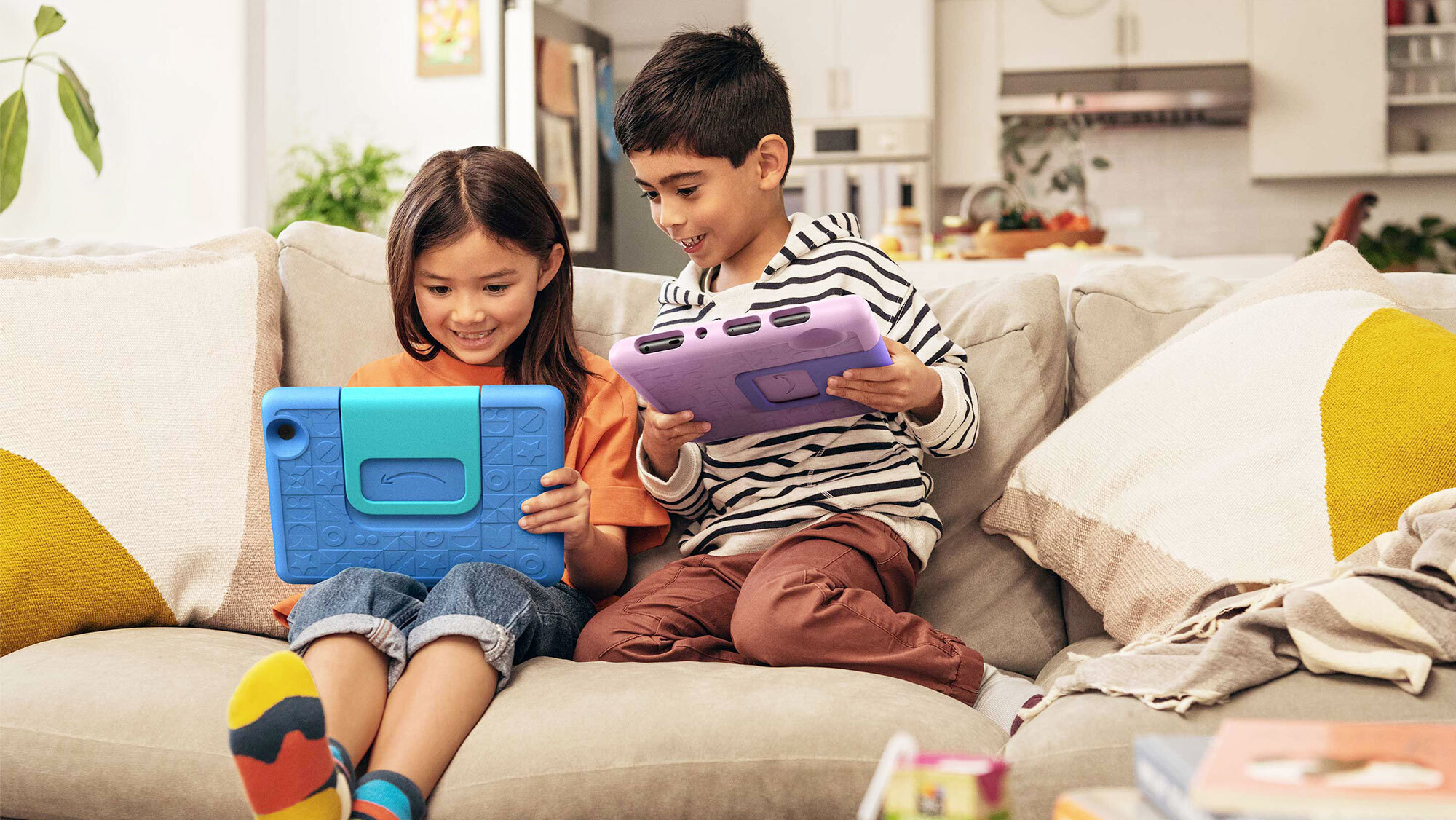 An image of two kids playing with their tablets sitting on a sofa. 