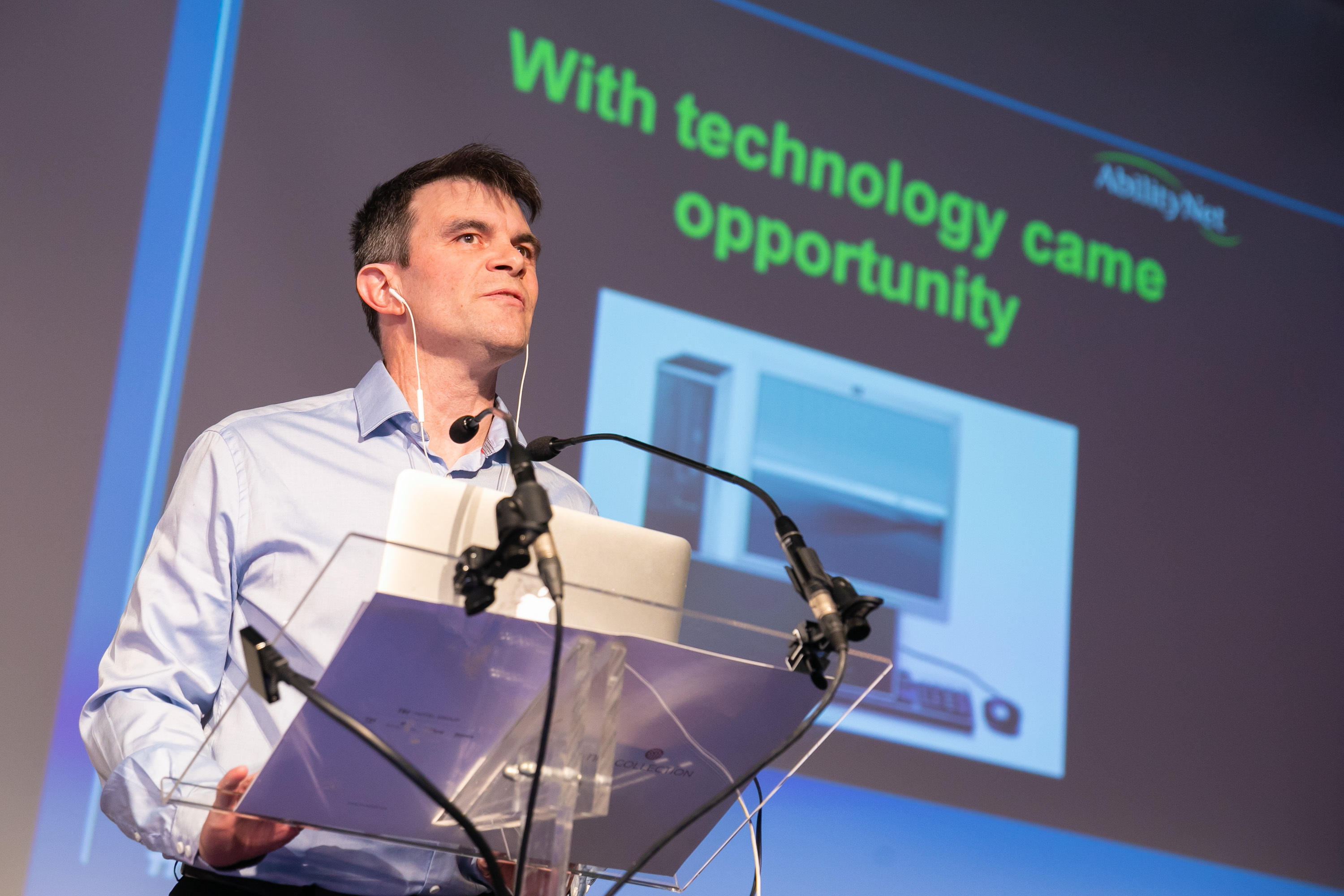 A close up image of Robin Christopherson standing at a glass podium giving a presentation.
