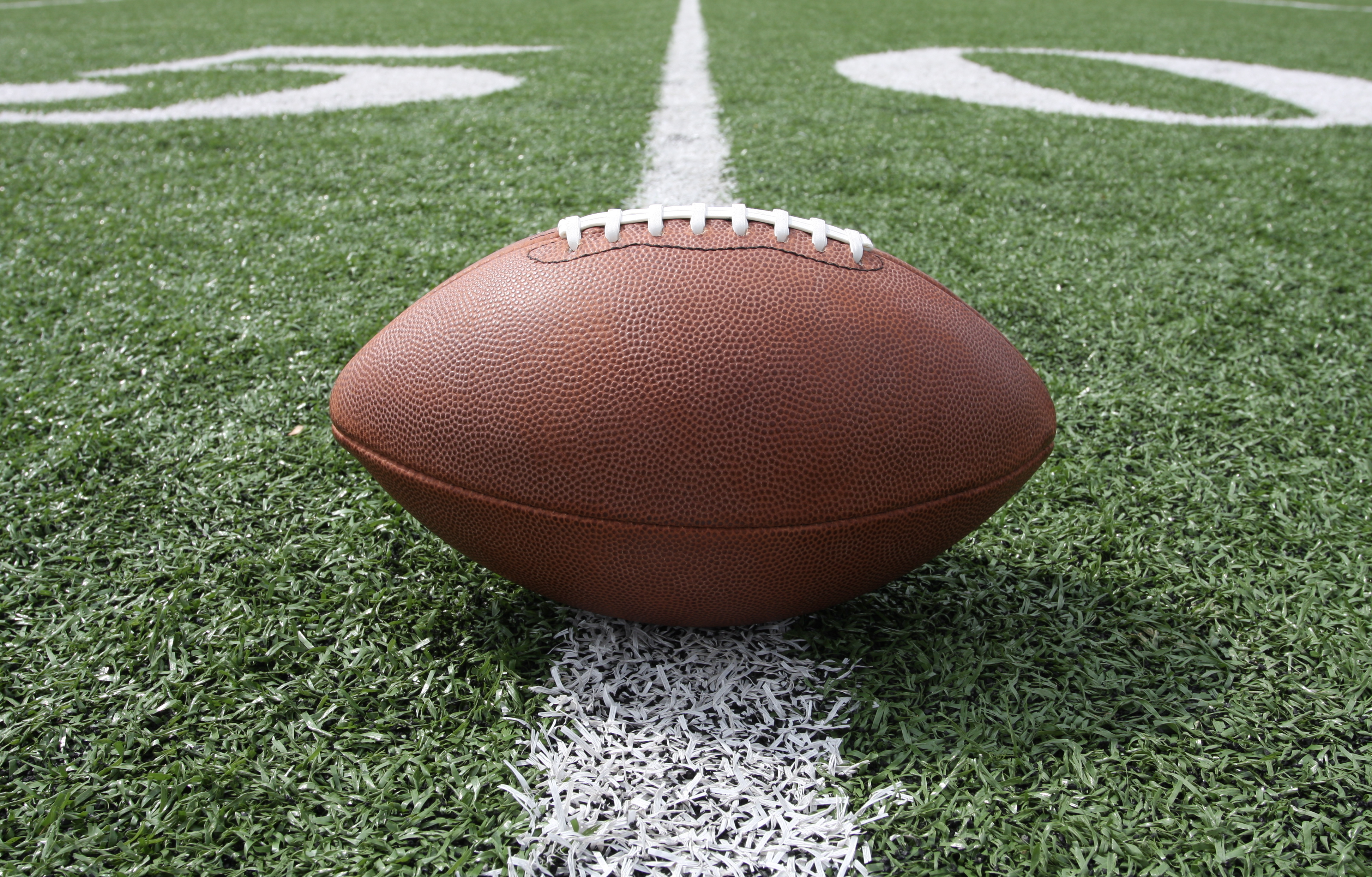 An image of a football sitting on top of a green football field with white yard markings.