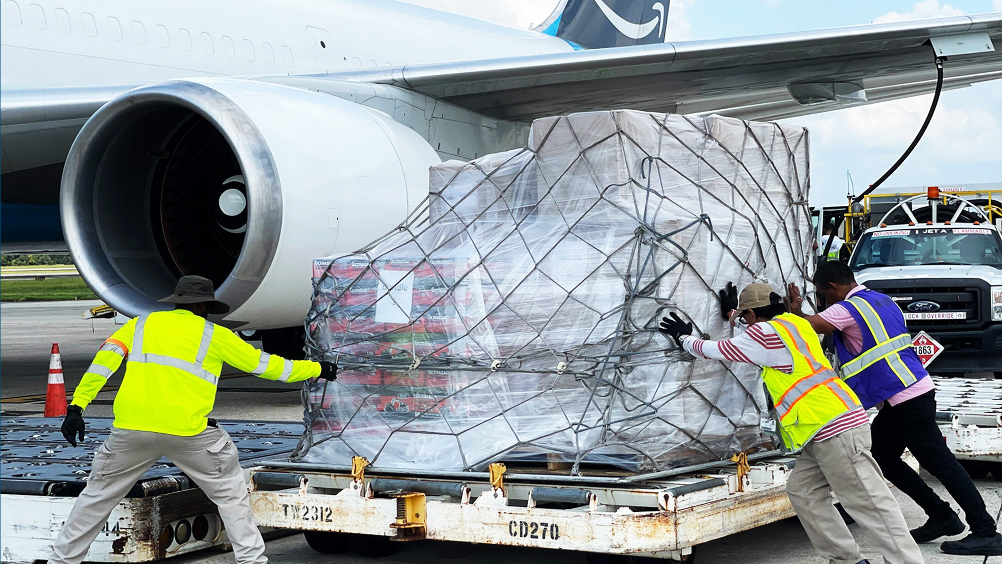 Amazon employees push a large cart of relief supplies toward a plane loading dock.