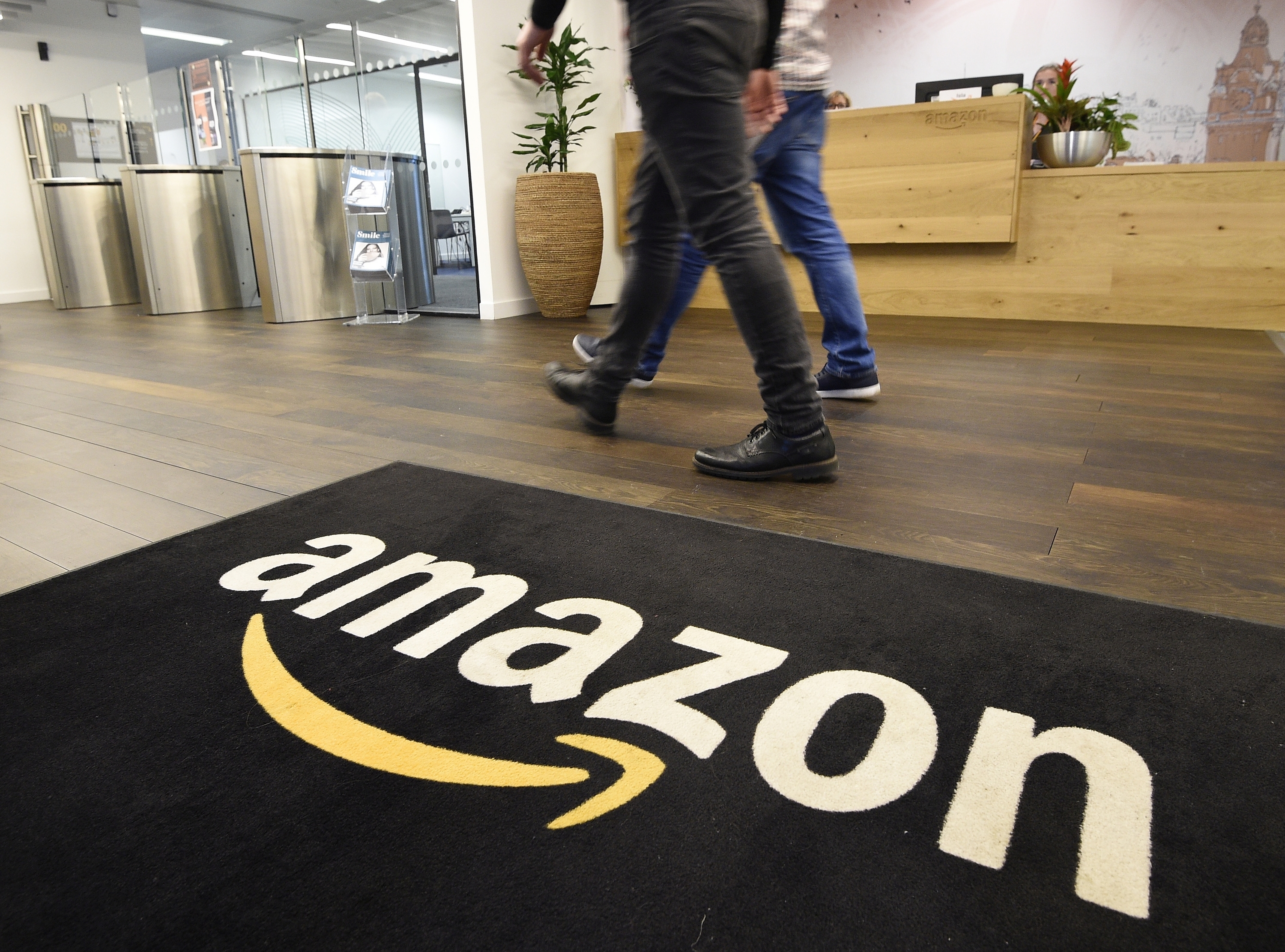 Amazon Development Centre Scotland mat with the amazon logo, two people are walking next to it.