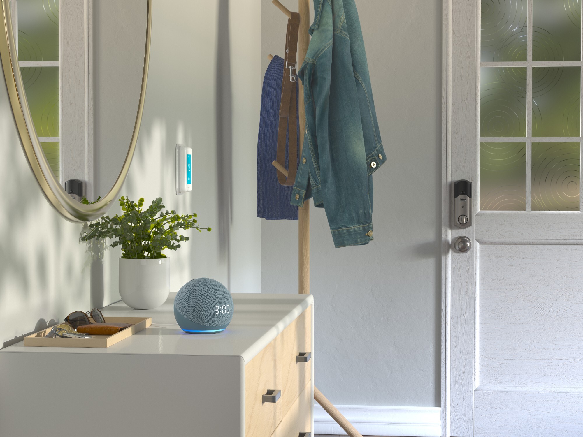 An entryway of a home has a coat rack as you walk in the door. There is a dresser with a mirror on the wall behind it. On the dresser is a Amazon Dot showing the time, a small plant and a tray holding keys, sunglasses and a wallet.