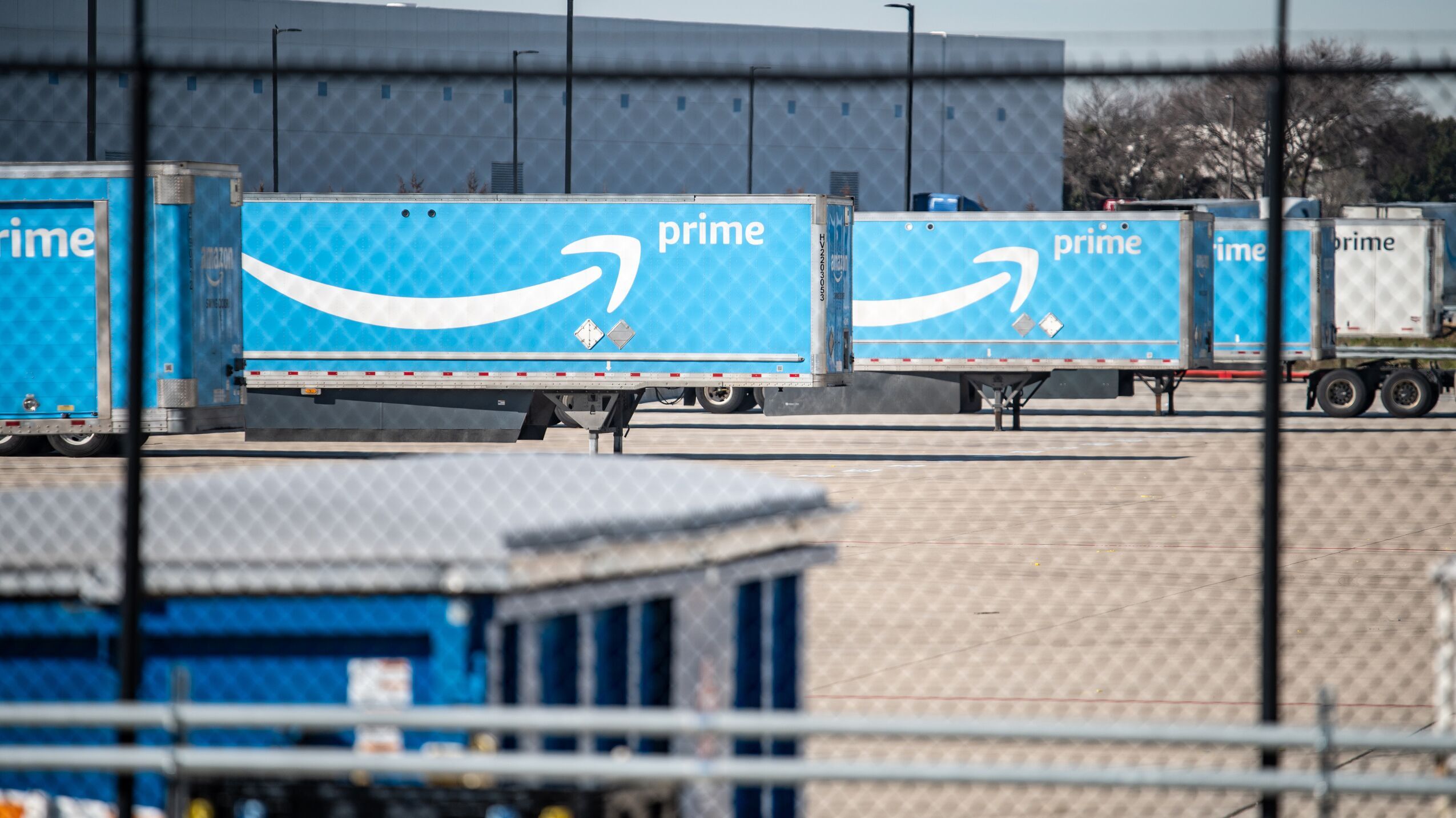 An image of a line of semi truck trailers lined up in a row at an Amazon Air hub. The trailers are light blue with white lettering that says "Prime" and large white Amazon smile logos.