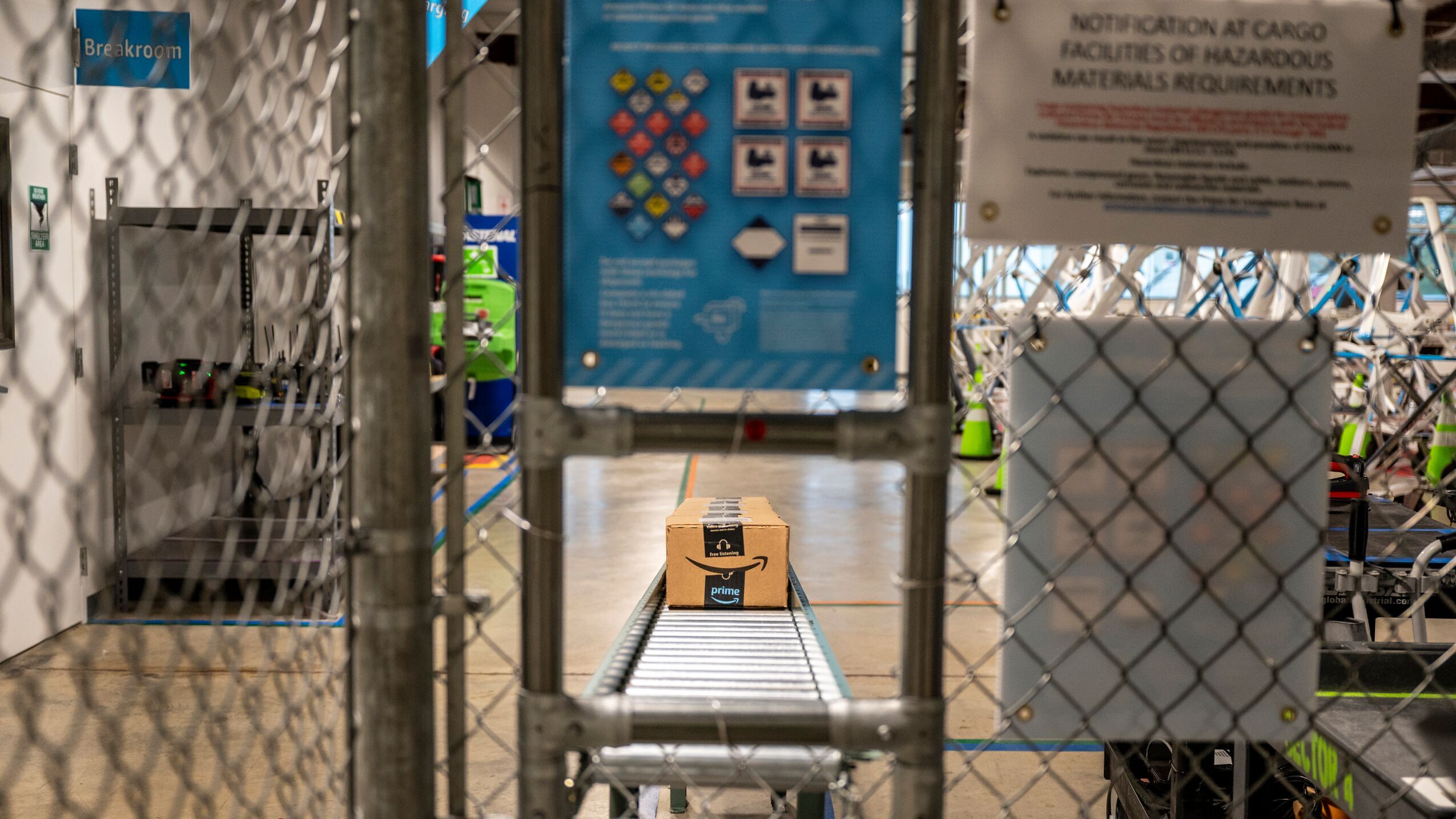 A peek through a fence looking at a package that is moving along a belt. 