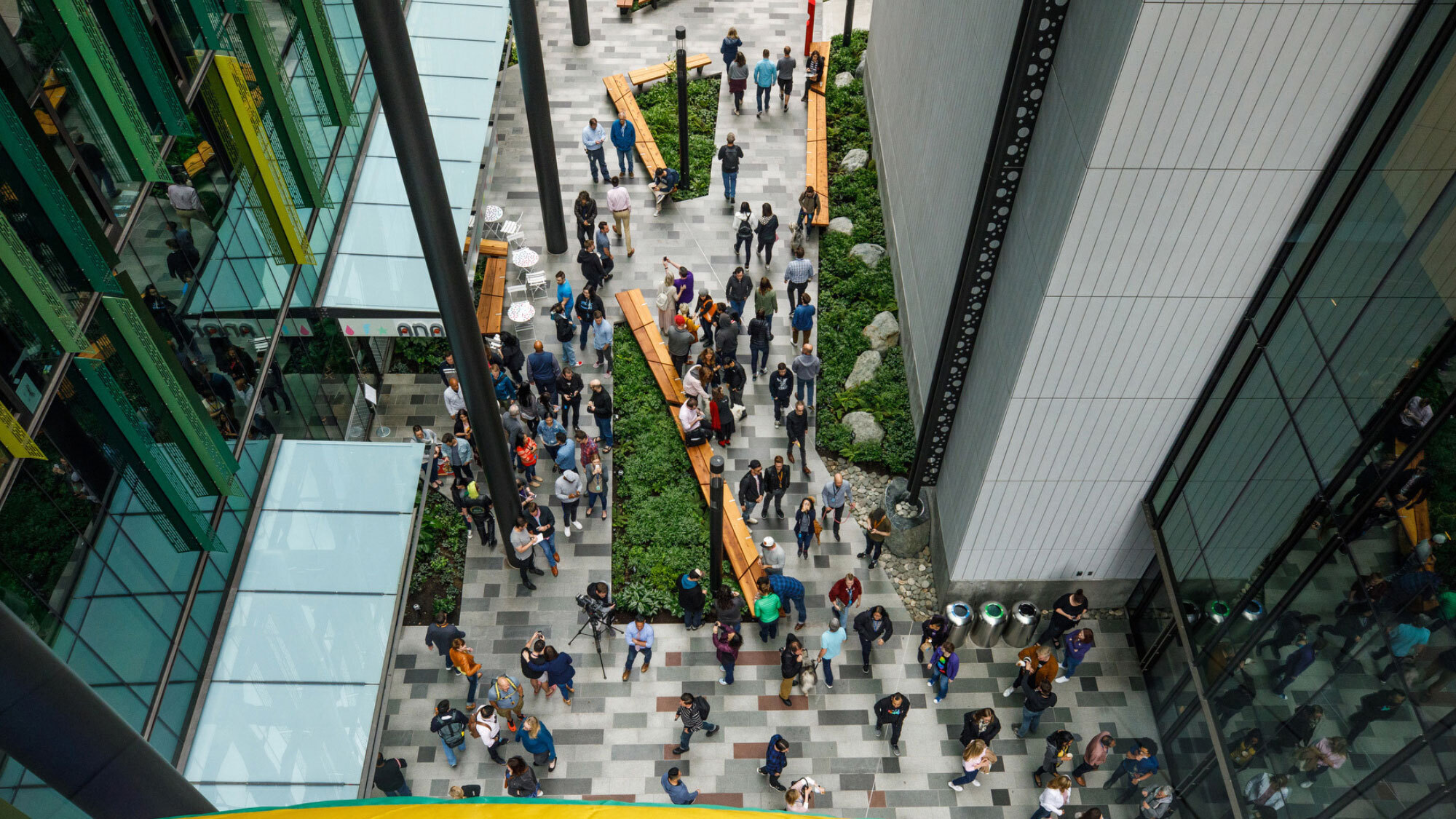 An image of the breezeway between buildings at Amazon's headquarters in Seattle. There are lots of people around on the ground and the camera is looking down from a bird's-eye view.