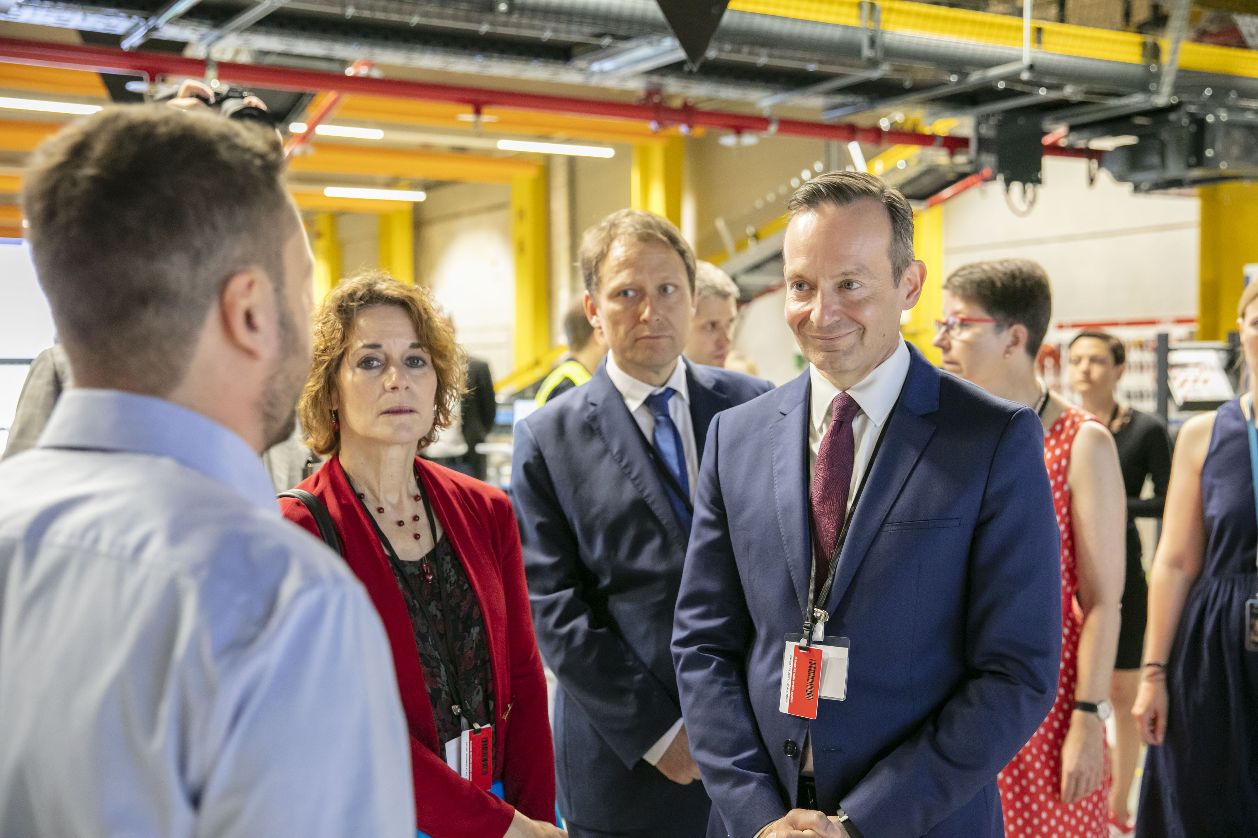 Standortleiter Johannes Weingärtner (im Rücken zu sehen) erklärt Oberbürgermeister Hebich und Landesminister Wissing die Abläufe. Im Hintergrund sieht man weitere Gäste sowie Teile der Logistikhalle.